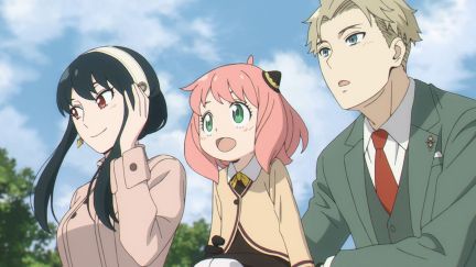 The cast of the anime series 'Spy x Family.' (l-r): Yor Briar (woman with long dark hair), Anya (young girl with a pink bob and bangs wearing a school uniform), and Loid (man with short blond hair wearing a 3-piece suit) are standing at a railing (Anya is sitting on the railing) looking out at something.