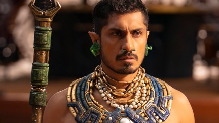 Image of Tenoch Huerta as Namor in Marvel's 'Black Panther: Wakanda Forever.' He is an Indigenous Mexican man with short dark hair with pointy ears and a thin beard. He's wearing green earrings, several beated necklaces and a large blue and gold neck adornment, and he's holding a green and gold spear.