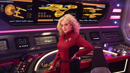 Pelia (Carole Kane) poses in a red Starfleet uniform on the bridge of the Enterprise.