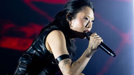 Rina Sawayama leans over and belts into a microphone, wearing black leather.