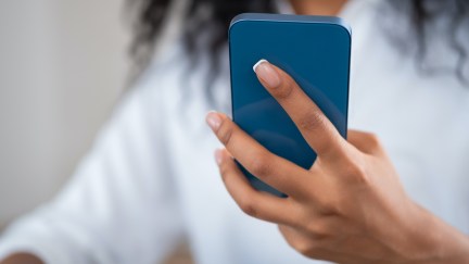 A woman with her face obscured holds her cell phone in front of her, looking at it.