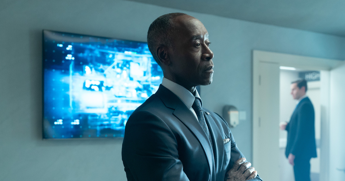 Rhodey folds his arms, looking unimpressed, with a TV screen behind him in Secret Invasion.