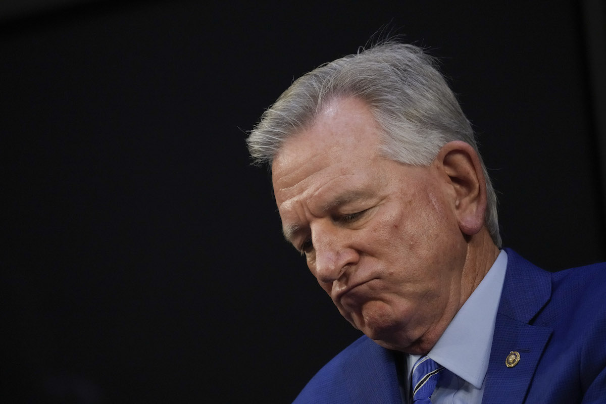 An old white man (Tuberville) sucks his bottom lip and looks sad.