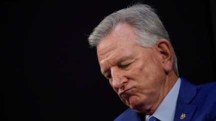 An old white man (Tuberville) sucks his bottom lip and looks sad.