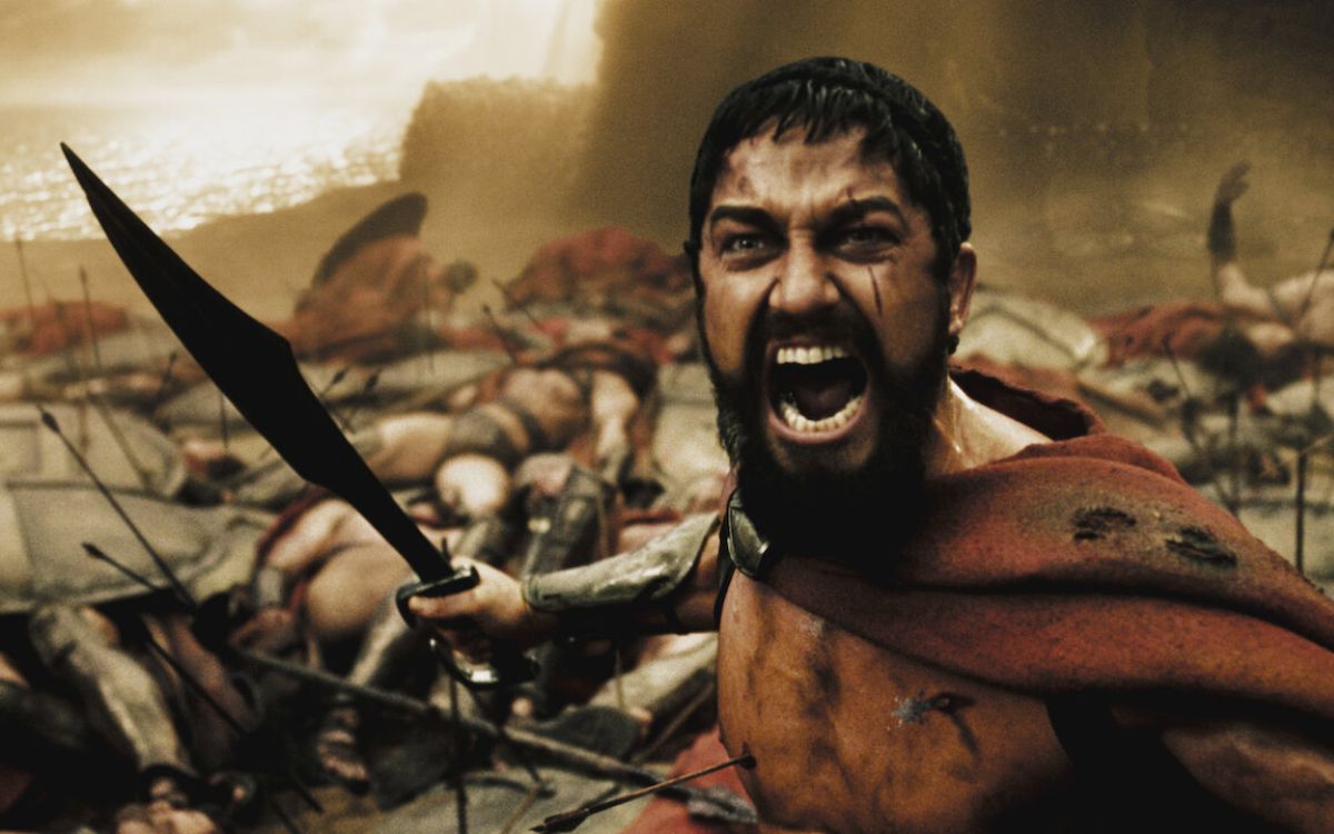 A man stands yelling loudly while holding a sword surrounded by bodies in "300"