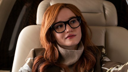 Julia Garner as Anna Sorokin/Anna Delvey in 'Inventing Anna.' She is a stylish young woman wearing glasses, seated in a leather chair