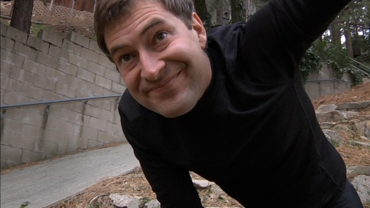 Mark Duplass in 'Creep': A man in a black turtleneck looks directly into the camera. His smile is unsettling. 