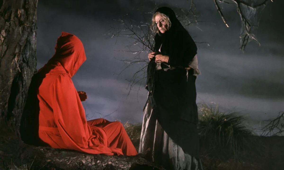 An old women talks to a red clad figure in the lonely woods