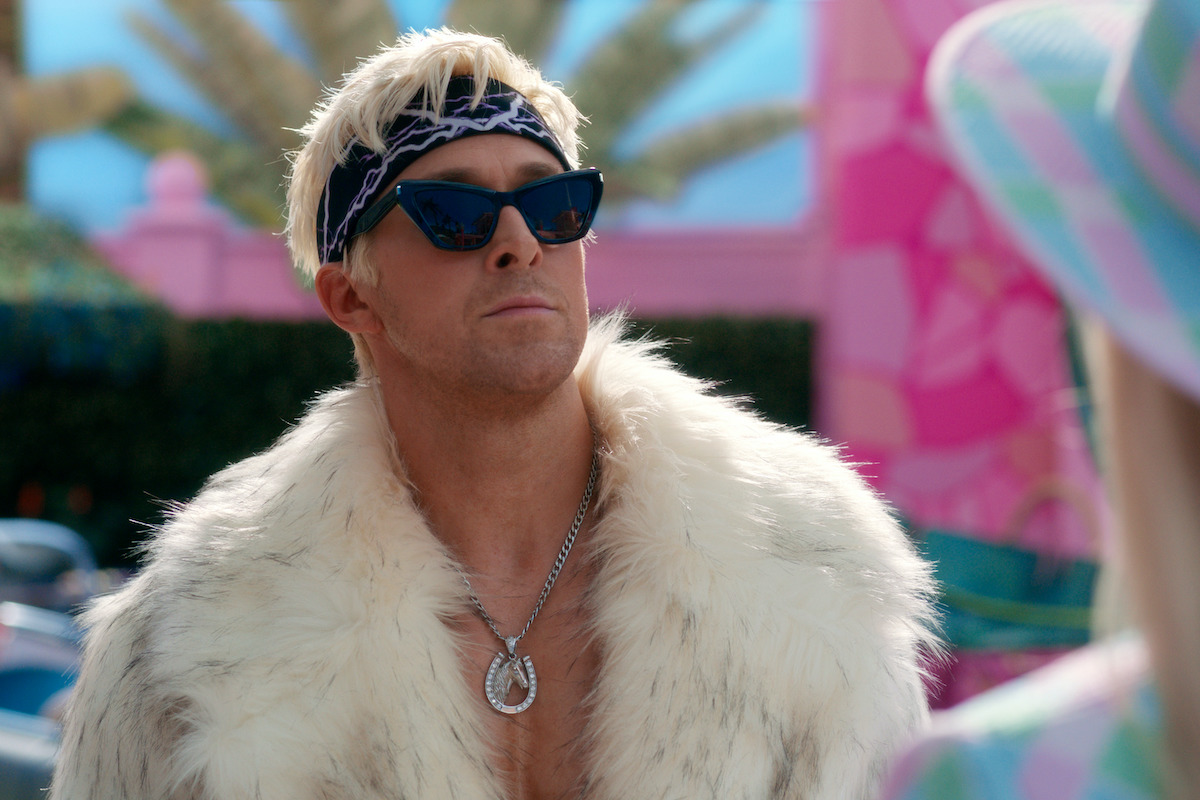 Ryan Gosling as Ken in the movie Barbie, wearing a white fur coat and sunglasses, mugging.