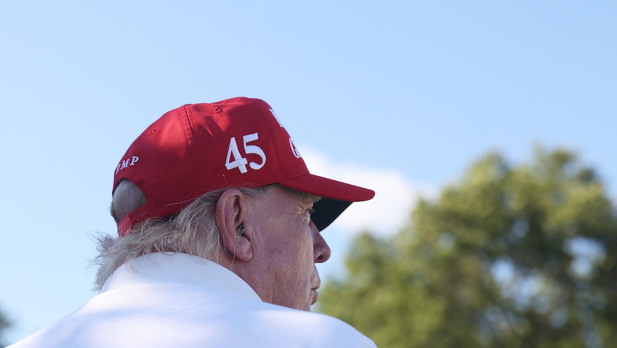 Donald Trump, seen from behind from the shoulder up, wearing a red baseball cap bearing the number 45.