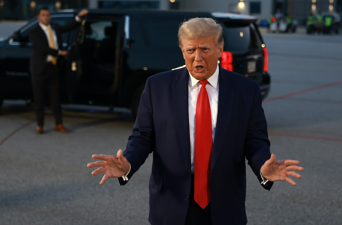 Donald Trump gestures and speaks to reporters outside.