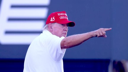 Donald Trump, looking off to the side and pointing, wearing his fascist hat.