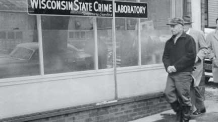 A black and white photograph of Ed Gein walking by a sign reading Wisconsin State Crime Laboratory