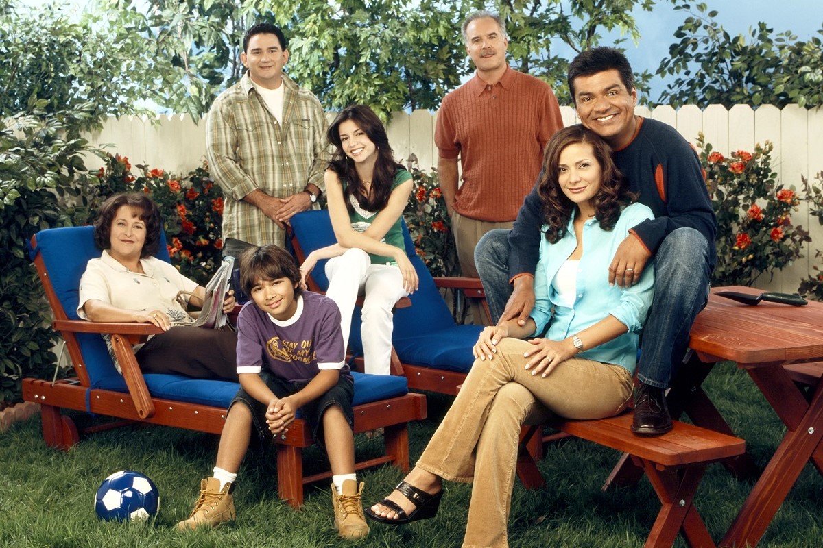 Promotional image of the cast of ABC's 'The George Lopez Show.' They are sitting in a backyard on patio furniture and a picnic table. 