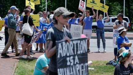 An abortion rights protester stands with a group of anti-abortion protesters behind her.