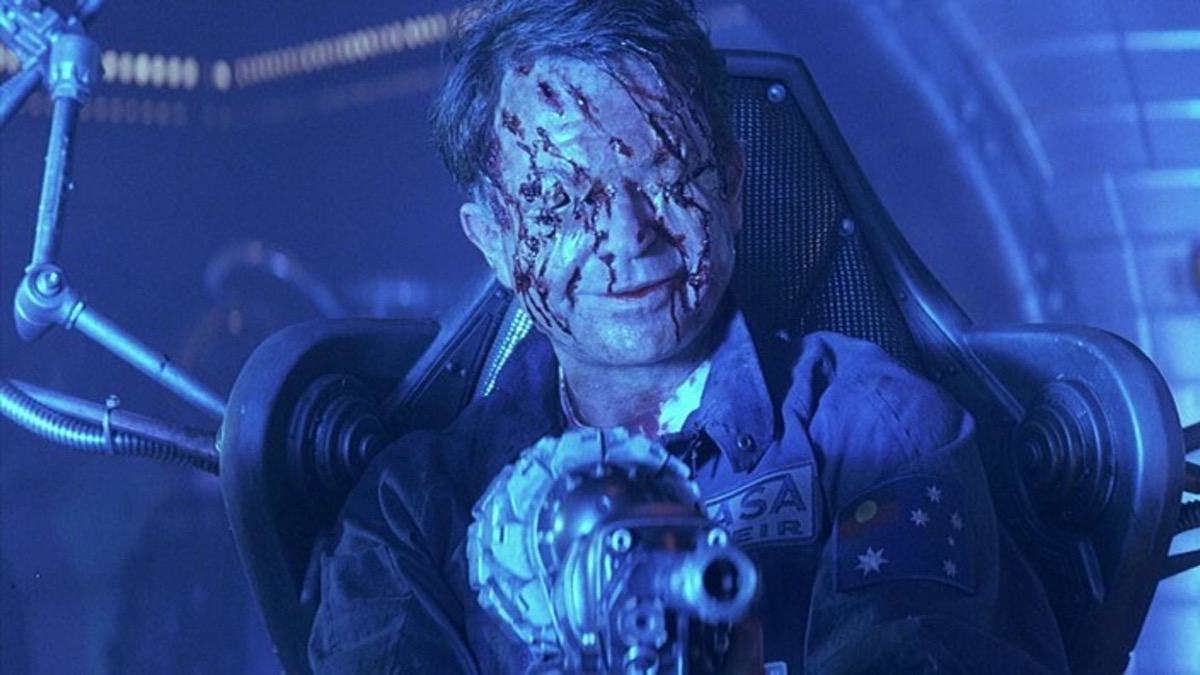 A man covered in cuts sits in a chair holding a weird gun in "Event Horizon"