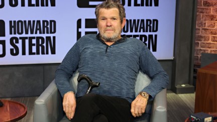 Jann Wenner on the Howard Stern Show. He reclines in a chair, looking somewhat uncomfortable.