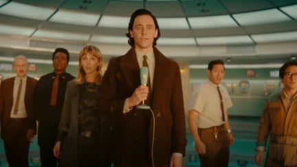 Loki holds a microphone, with Mobius, B-15, Sylvie, Casey, and O.B. standing behind him.