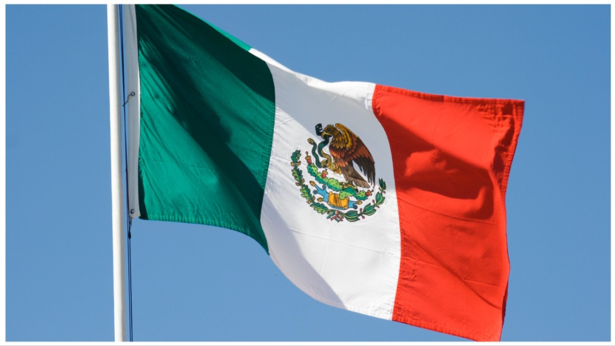 Horizontal view of a Mexican national flag waving in the wind against a clear blue sky.