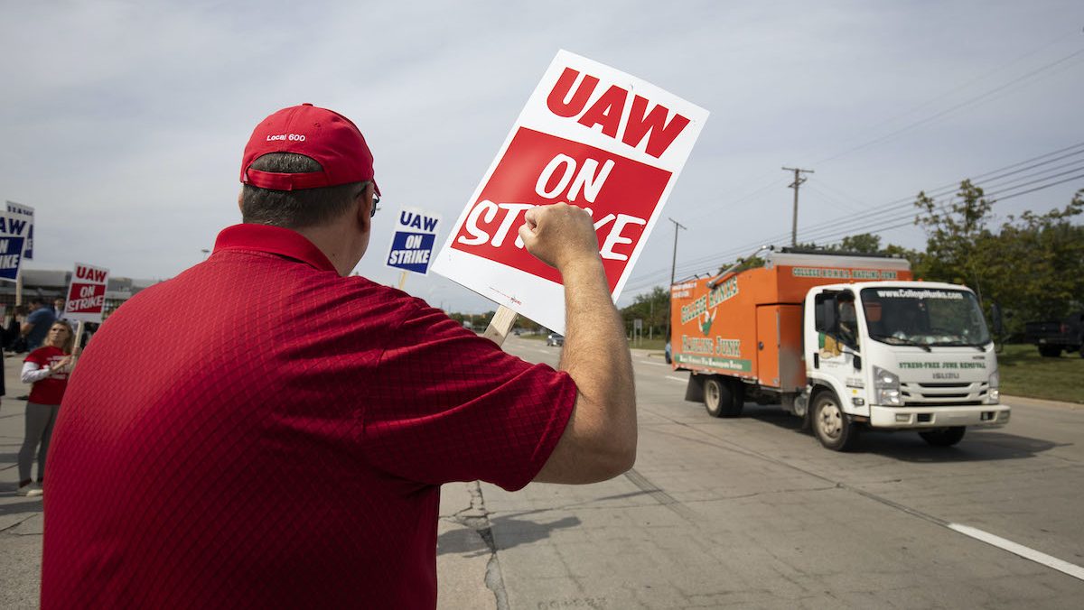 A man holding a UAW on Strike sign raises his fist to passing cars.