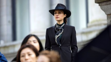 A woman (Carla Gugino) stands in above the crowd wearing black hat and trench coat in 'The Fall of the House of Usher.'