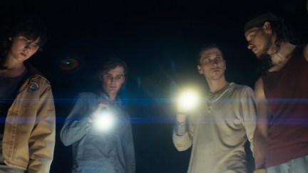 Four young people look down at the ground with flashlights against a black sky.