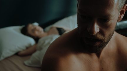 A post-coital Axel (Shane Quigley-Murphy) sits in the foreground with an undressed Dakota (Paige Gilmour) in the background in ‘Kill Your Lover.’