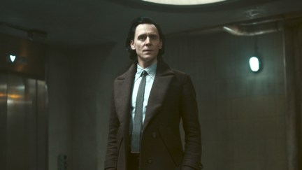 Loki stands in a dark hallway in the TVA, looking concerned.