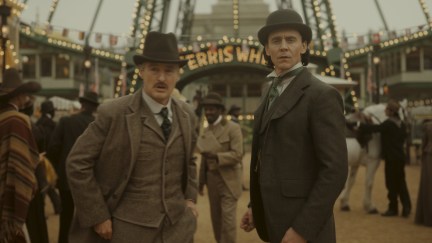 Mobius and Loki standing in front of the ferris wheel at the 1893 World's Fair. They're both in period costume.