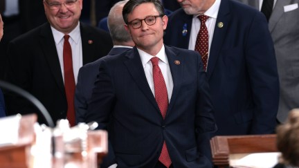 Mike Johnson has his hands in his pockets giving a thin-lipped smile on the House floor.