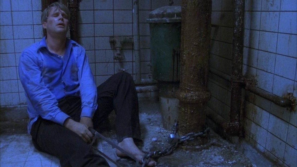 A man with his foot chained to the floor of a bathroom looks miserable in "Saw"
