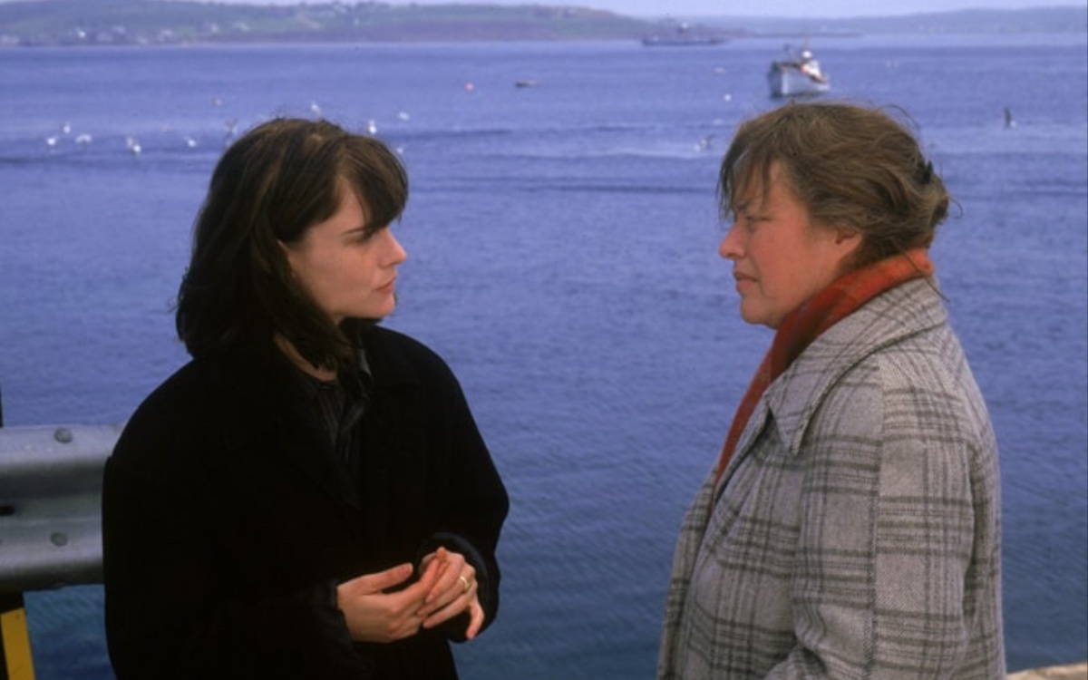 On the right is Jennifer Jason Leigh as Selena St. George and on the left is Kathy Bates as Dolores Claiborne in Dolores Claiborne; the two caucasian women are talking to each other next to the ocean