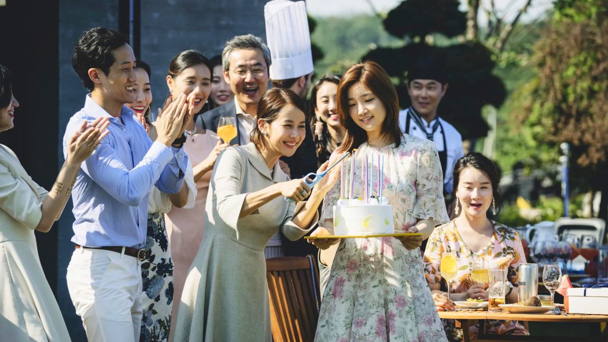 A group of South Korean party goers gather around a young woman holding a cake in Parasite.