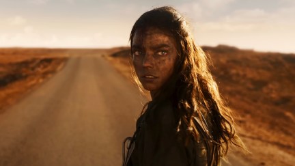 Furiosa (Anya Taylor-Joy) looks over her shoulder at the camera with a desert highway in front of her.