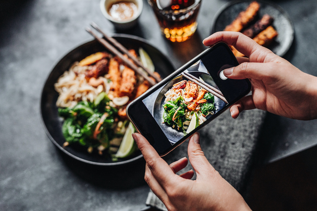 Hand of a chef taking photograph of a dish on table with a mobile phone.