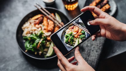 Hand of a chef taking photograph of a dish on table with a mobile phone.