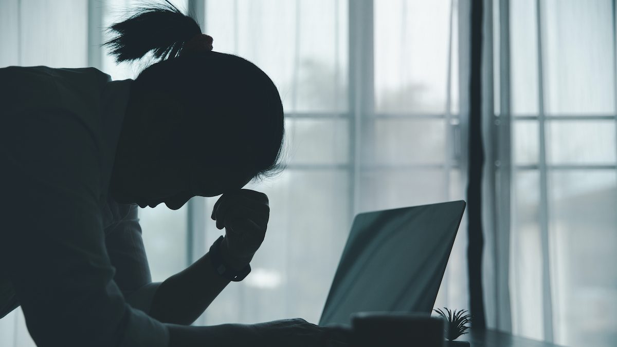 Seen in shadow, a woman looks distressed over a laptop.