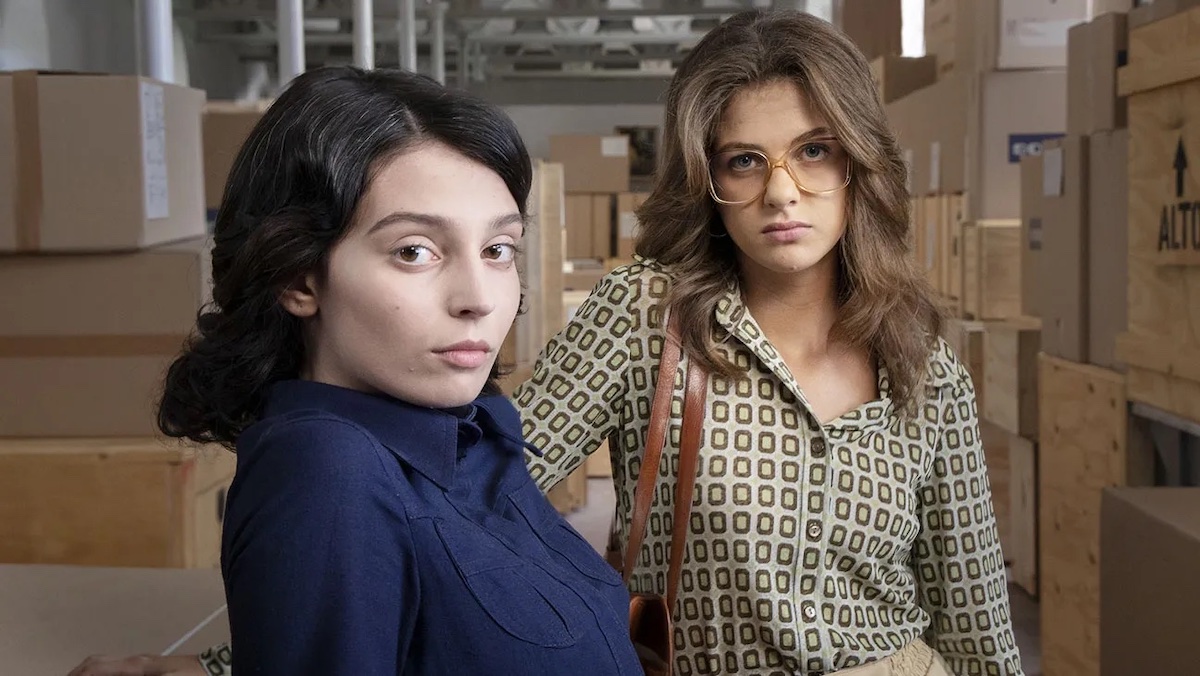 Lila and Elena pose against a backdrop of cardboard boxes in My Brilliant Friend