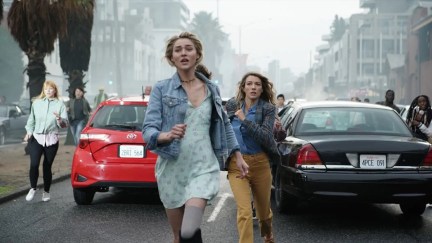 A young woman and a teenager run through chaos in the streets in 