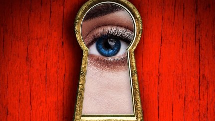 A woman'e eye peers through a keyhole against a red background