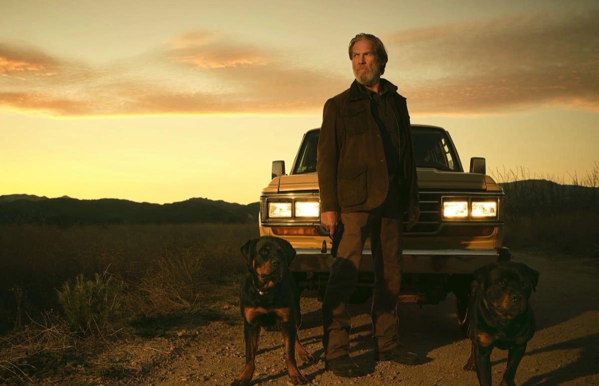 An old man stands in the desert in front of a truck with two dogs in "The Old Man"