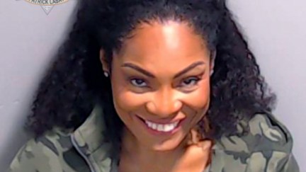 A Black woman (Kutti) gives a Joker-esque smile in a police mugshot