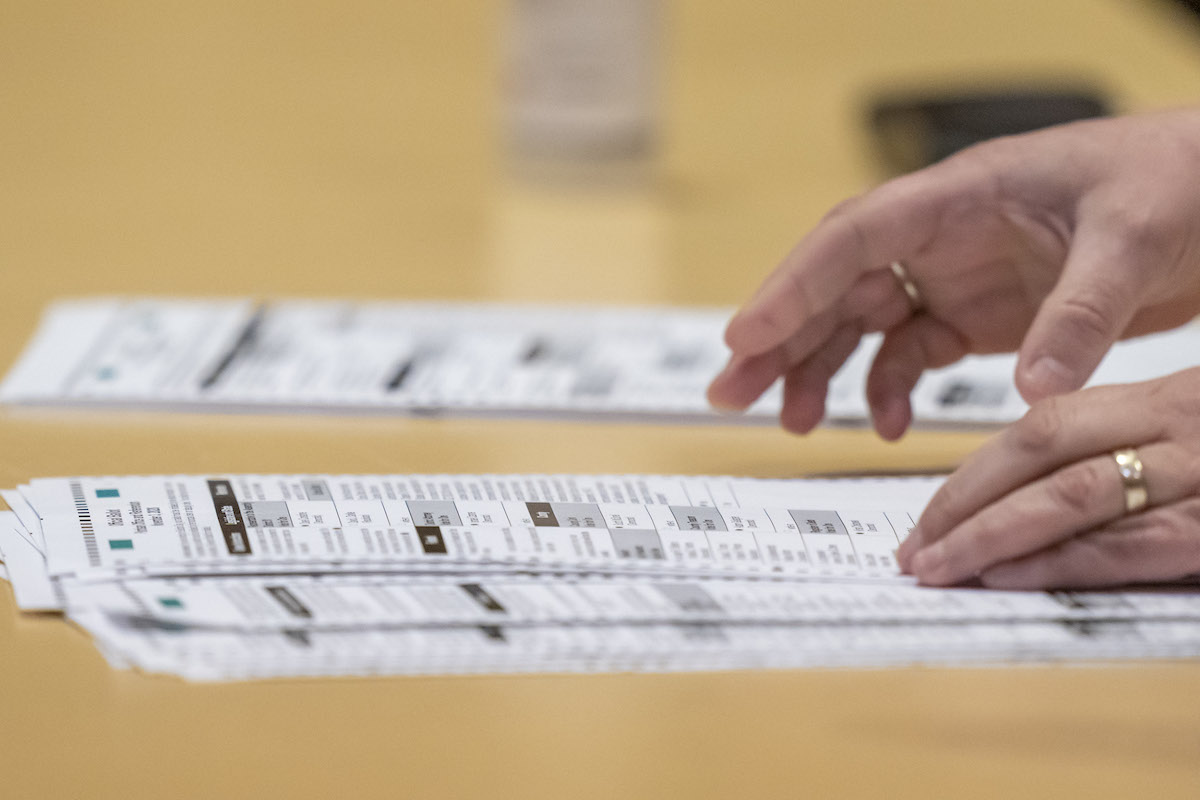 Hands sorting piles of election ballots on a table.