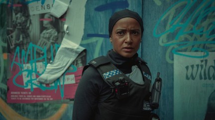 Image of Amaka Okafor as DS Hasan in Netflix's 'Bodies.' She is a Black Muslim woman with her hair covered and wearing a black police uniform. She is standing in front of a blue, graffiti covered wall.