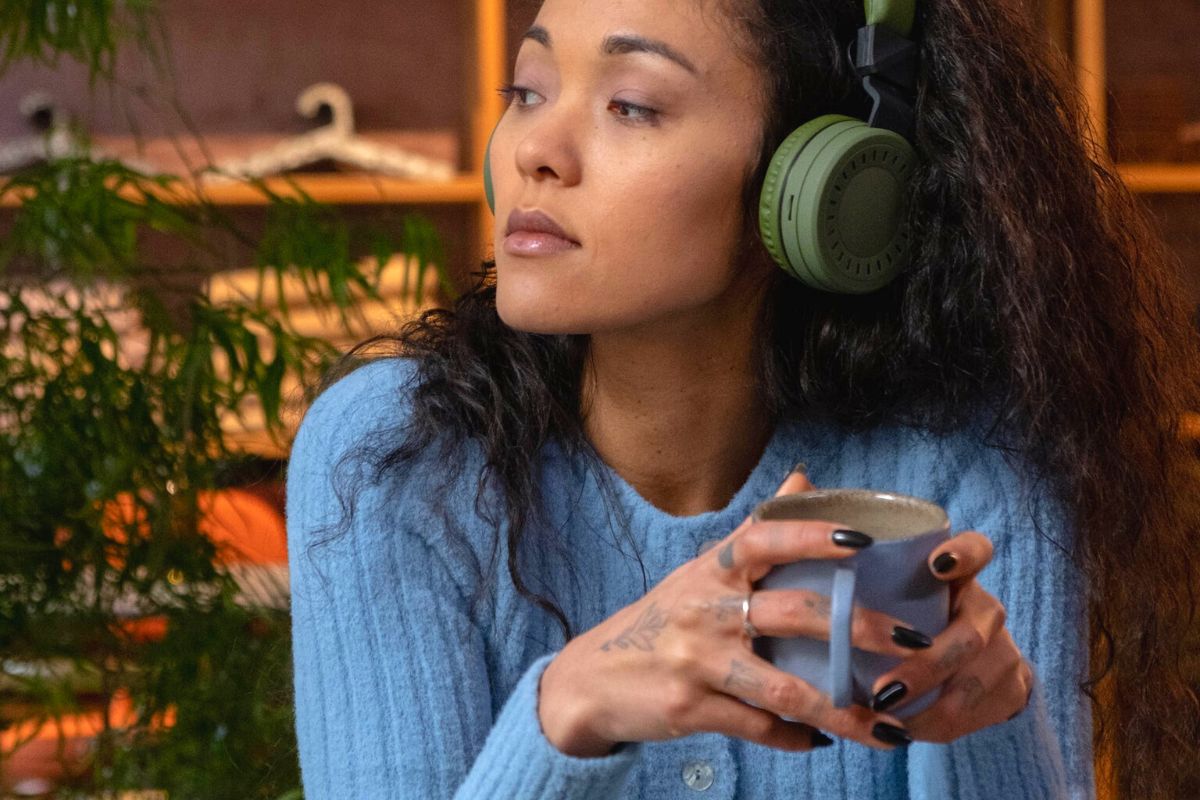 Woman listening to something on her headphones while sipping on something in a mug. Maybe an audiobook or the newest Janelle Monae album. 