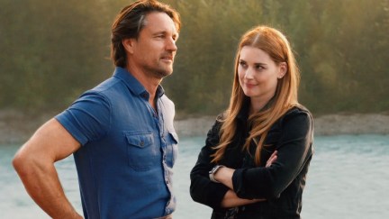 A man and woman stand on the edge of a sunlit lake in 