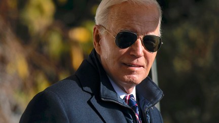 Joe Biden gives a slight smile to the camera, wearing a coat and aviator sunglasses.