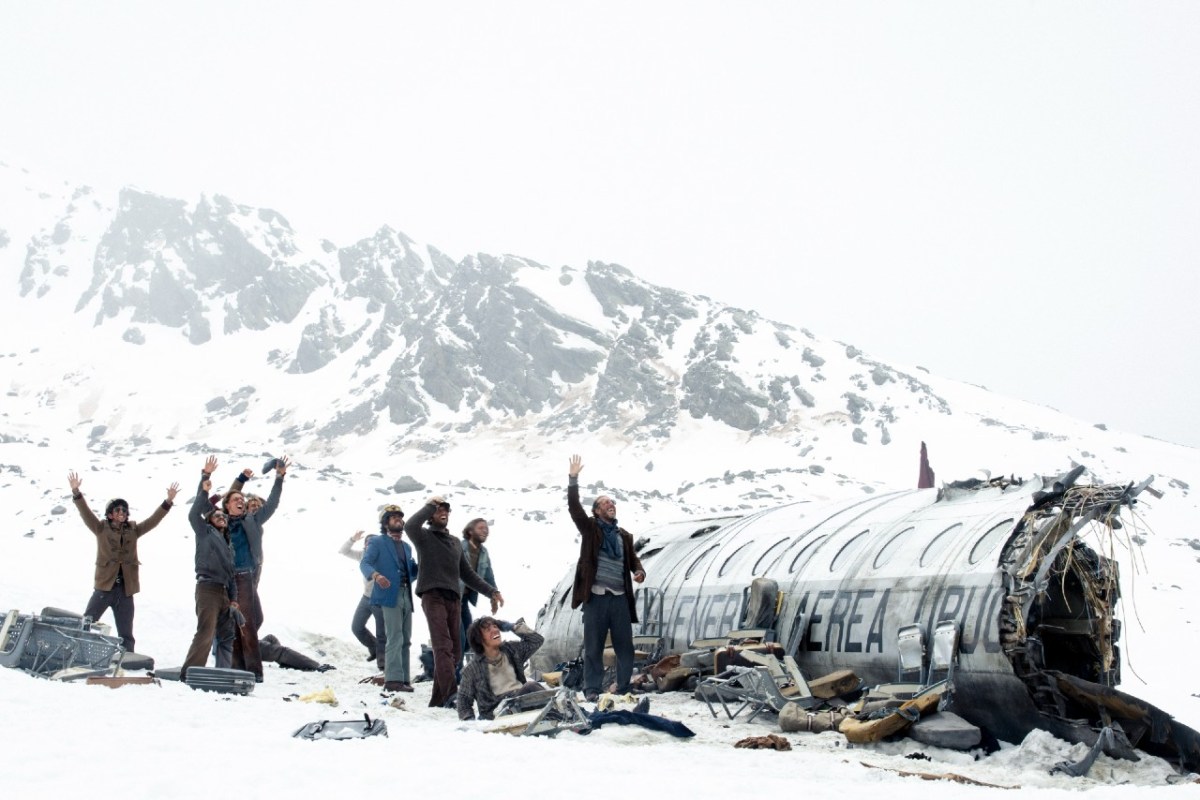 Men stand in the snow beside a wrecked airplane in 'Society of the Snow'.