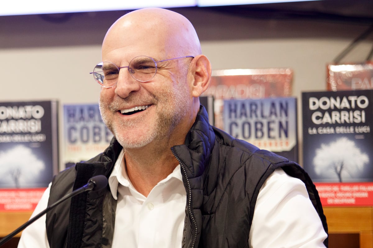 Harlan Coben sits at a microphone in front of a wall of his books.