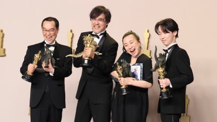 The visual effects team for Godzilla Minus One holds up their Oscars and toy Godzillas.